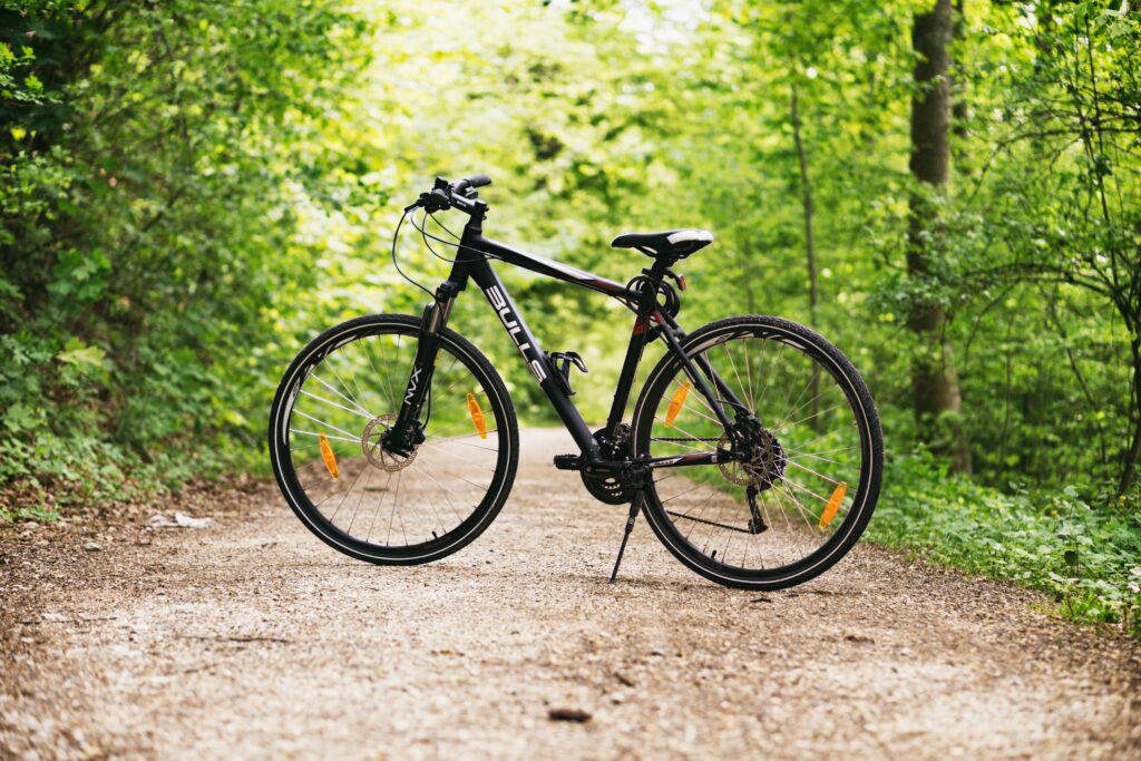 A mountain bike resting on a forest path surrounded by lush green trees in broad daylight.